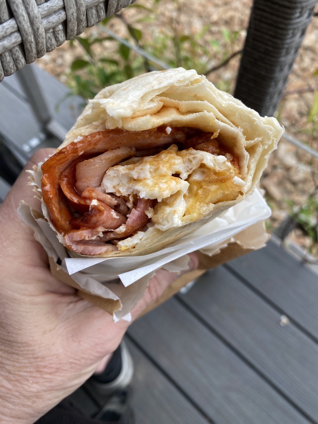 A breakfast wrap held in a hand, filled with bacon and scrambled egg