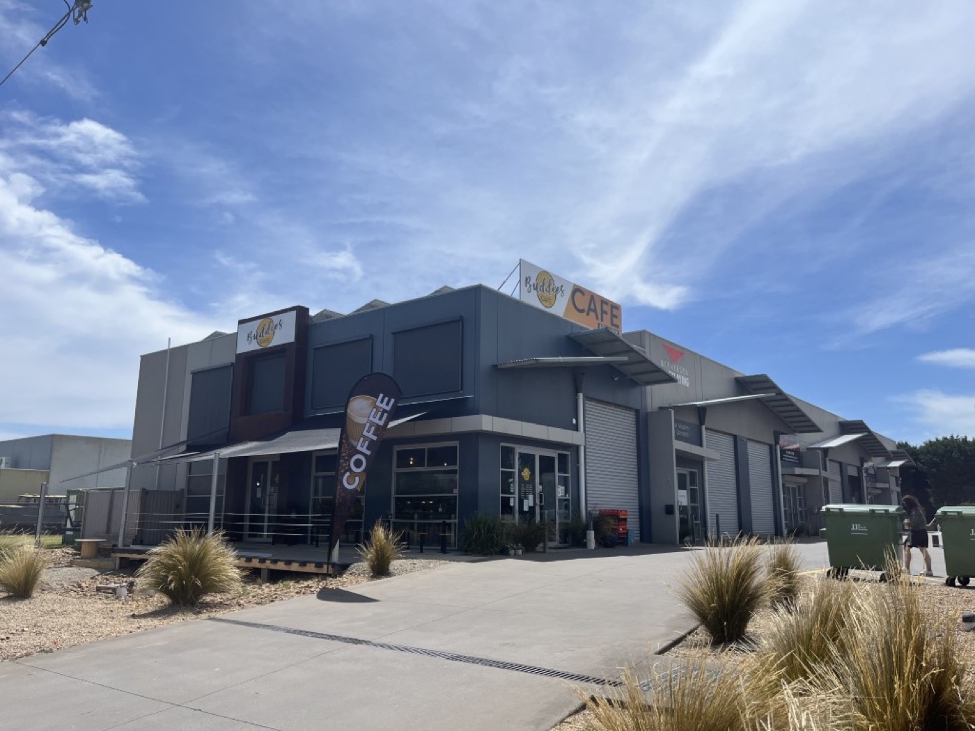 The cafe's grey industrial-style building with a Coffee banner out front, seen from the car park under a blue sky