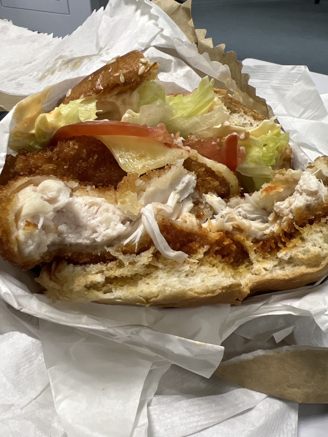 A crumbed chicken schnitzel roll in paper, with cheese, tomato and lettuce
